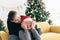 Young Asian man surprises and closes her eyes with a Christmas gift at home with a Christmas tree in the background.