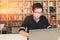 Young Asian man working on laptop at home office or library with serious face, bookshelf with clock blur background with clock