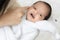 Young Asian mother hugging a cute newborn baby smiling in white bedroom. Duty of the wife to raise children. Mother and child