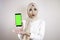 Young Asian Muslim beautiful girl wearing head scarf is shocked showing green screen smartphone