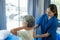 A young Asian nurse at a nursing home takes care of a senior woman. The attending physician provides physical therapy services