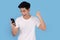 A young Asian person is wearing a white T-shirt, smiling and happy to celebrate while looking at mobile phone on a blue background