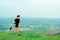 Young Asian runner, wearing black sportswear, running on a big mountain trail, cool morning, windmills, and sky in the background