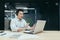 A young Asian salesman is sitting in a headset in the office at a table in front of a laptop