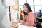 Young Asian seamstress in casualwear sitting by workplace inside large contemporary workshop