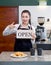 Young asian shopkeeper with a smile holds an OPEN sign in front of a coffee shop counter. Morning atmosphere in a coffee shop