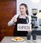 Young asian shopkeeper with a smile holds an OPEN sign in front of a kitchen counter. Morning atmosphere in a coffee shop