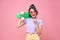 Young asian teenage girl holding skateboard with lollipop on pink background