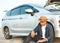 A young Asian tourist has driven a car and broke down on the way. He sat down on the floor beside the wheel of a car