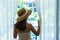 Young Asian traveler woman with straw hat looking outside the window in hotel room after check-in. Travel and summer holiday conce