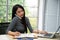 Young Asian woman calling telephone and taking memo while using laptop