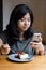 Young asian woman chating mobile phone with a cake