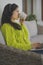 Young asian woman drinking cup of tea while resting on the balcony sofa with laptop