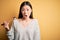 Young asian woman eating japanese food, holding salmon and rice maki sushi using chopsticks scared in shock with a surprise face,