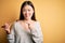 Young asian woman eating japanese food, holding salmon and rice maki sushi using chopsticks very happy pointing with hand and