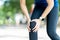 Young asian woman holding knee pain in running public nature park in the morning. Joint injury in athlete or jogger concept with