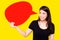 Young Asian woman holding red speech bubble on yellow background. Asian female show sign speech bubble banner, pretty girl look at