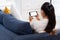 Young asian woman holding smartphone with blank white screen ,lying down cozy on sofa in living room,technology mockup  gadget