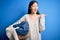 Young asian woman holding wicker laundry basket doing domestic chores pointing and showing with thumb up to the side with happy