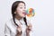 Young Asian woman licking a multicolored lollipop against white background