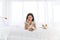 Young asian woman lying in white bed with maltese and white Shiba Inu puppy, Cheerful and nice couple with people and pet.