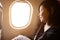 Young asian woman on passenger seat near window in airplane..Traveller sitting inside plane at the airport with sky and sun light