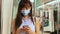 Young Asian woman passenger wearing surgical mask and listening music via mobile phone in subway train