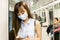 Young Asian woman passenger wearing surgical mask and using mobile phone in subway train