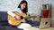 Young Asian woman practicing and learning how to play guitar on laptop computer monitor. Female guitarist watching