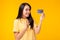 Young asian woman showing plastic credit card and looking at credit card with excited and happy stand over yellow background