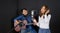 Young asian woman singing in front of black soundproofing wall. Her boyfriend played the guitar together. Musicians producing