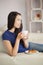 Young asian woman sitting on the sofa having coffee with a pastry