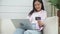 Young asian woman sitting on sofa using laptop computer shopping online with credit card buying to internet.