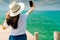 Young Asian woman wear straw hat in casual style use smartphone taking selfie at wooden pier. Summer vacation at tropical paradise