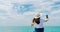 Young Asian woman wear straw hat use smartphone taking selfie at wooden pier. Summer vacation at tropical paradise beach. Happy