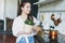 Young asian woman in white shirt hold basket with green house plant in wicker pot in hands at the kitchen