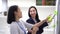 Young Asian woman writing ideas on white board while middle age woman is watching indoors