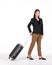 Young asian women in black suit smiles as she walks dragging a black suitcase. Portrait on white background with studio light