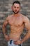 Young athlete posing with a torso for photography on a brick wall background. Bodybuilder, athlete with pumped muscles
