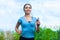 Young athlete running in the park and listens to music in summer, morning exercise.