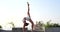 Young athlete woman in white sporty outfit doing acrobatics on the roof over sky background