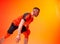 Young athletic basketball player in attack position holding ball with one hand on orange and red background