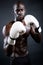 Young athletic boxer wearing gloves in black background.