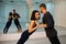 Young athletic couple in dark suits practicing pair yoga in studio with mirrors. Balancing in pair