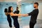 Young athletic couple in dark suits practicing pair yoga in studio with mirrors. Balancing in pair