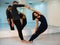 Young athletic couple in dark suits practicing pair yoga in studio with mirrors. Balancing in pair