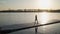 Young athletic girl goes down the pontoon along the lake on the background of beautiful sunset. Shooting on the Steadicam