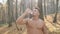 Young Athletic Guy With Naked Torso Stands In The Woods And Drinks Water.