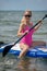 Young athletic woman in bright pink swimsuit doing fitness on a sup board with an oar on sea. Tropical travel and water activity