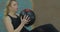 Young athletic woman doing abdominal press exercise works hands and feet uses ball dressed in black sportswear.